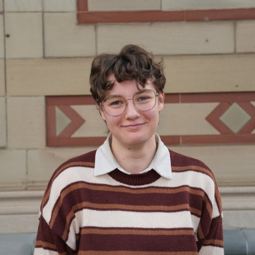 A headshot of a student wearing a brown and white striped sweater.