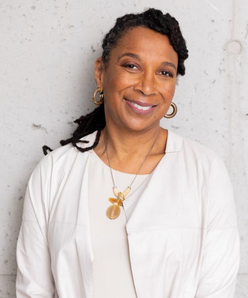 A waist-up headshot of scholar and author Kimberlé W. Crenshaw. She is wearing a white top, gold necklace, and has her hair tied back.