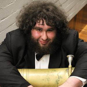 Bearded man in a tuxedo with a tuba on his lap