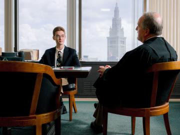a student wearing a suit coat speaks to a judge as the Cleveland skyline is visible behind them