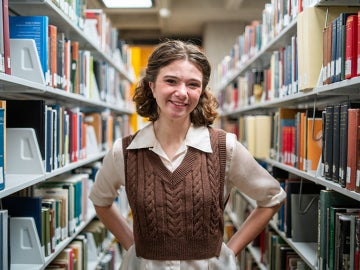Student smiles while standing in bookstacks