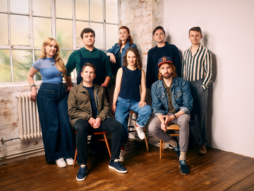 Eight people, standing near one another in corner of room