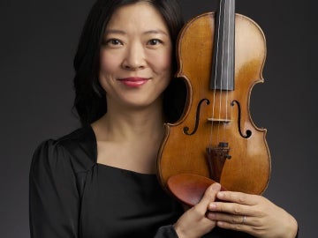 a smiling person holds a violin next to her face