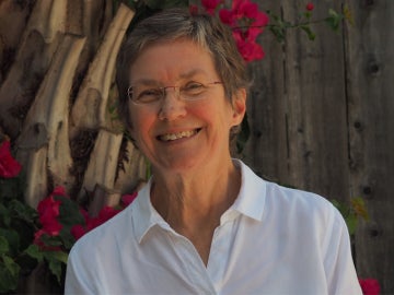 a person wearing a white collared shirt and glasses stands in front of magenta flowers