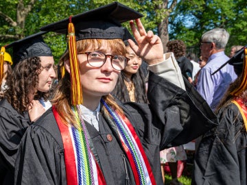 a person wearing a black graduation gown tips their fingers to a mortarboard