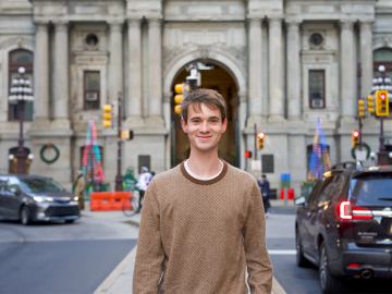 a smiling person stands in front of a building 