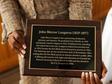 President Ambar holding a plaque that reads John Mercer Langston.