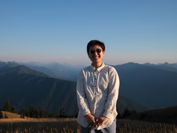 a person wearing sunglasses and a white shirt standing in front of beautiful scenery