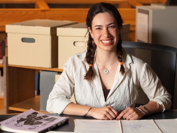 a smiling person wearing a white shirt and braids in a library