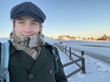 a person wearing a scarf and hat standing on a snowy road 
