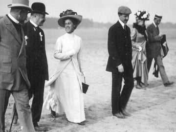 a person from the early 1900s wearing a white dress and hat walking with purpose