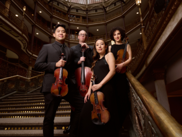 two men and two women stand on ornate staircase holding string instruments