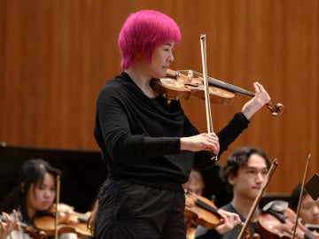a pink haired violinist plays with student musicians