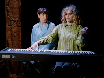 a person wearing a wig and a green top playing a piano