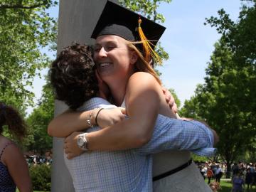 A woman wearing a commencement cap embraces another person outdoors