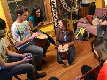Group of people seated in a circle playing music with an acoustic guitar and djembe drums.