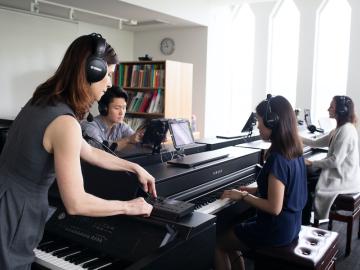 teacher working with students at keyboards in a piano pedagogy lab.