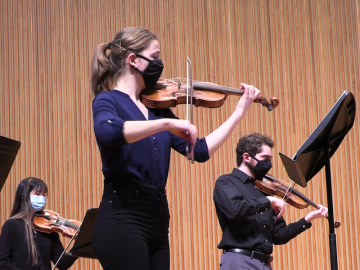 Baroque violinists performing onstage.