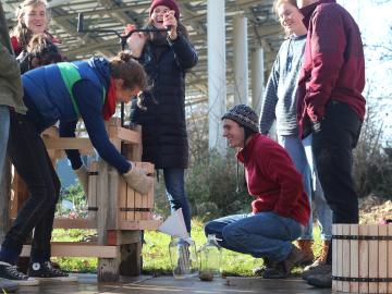 A group of students using a hand-cranked cider press.