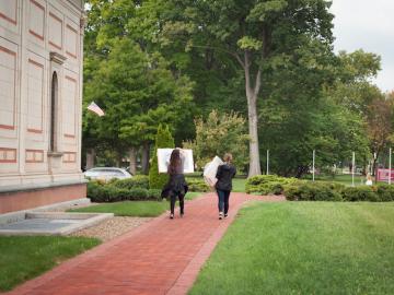 Two students walk away from the museum, each carrying a framed artwork.