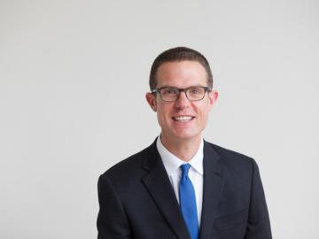 Bill Quillen man in navy suit and blue tie wearing glasses.