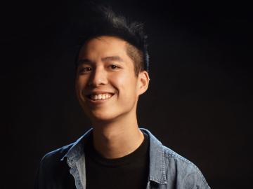 Asian man smiling and wearing a black shirt and jean shirt.