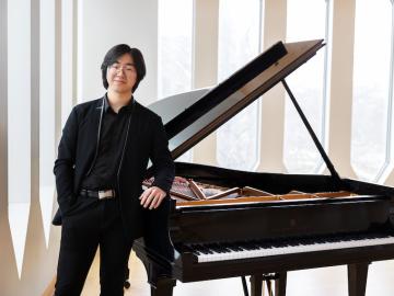 portrait of pianist Jiongli Wang standing in front of a grand piano
