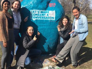 Five students in front of a blue painted rock