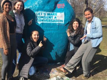Five students in front of a blue painted rock