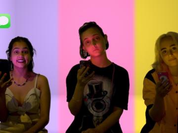 "CRSHD" movie still showing three main actresses looking at the camera, holding their phones, against purple, pink, and yellow background