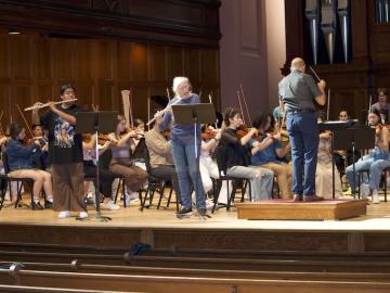 two flute soloists rehearse in front of an orchestra
