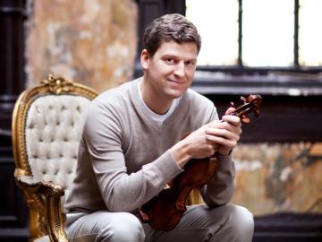 man sitting in cushioned chair holding violin