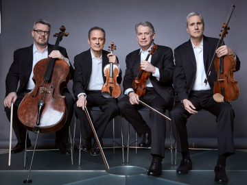 Four men in black suits sit next to one another holding string instruments