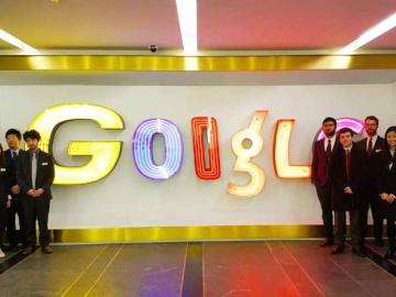 Groups of students stand before an electric Google sign