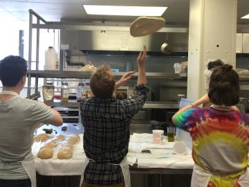 A student cook tosses and spins pizza dough.