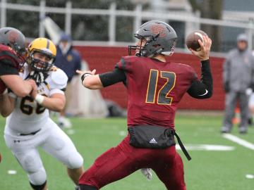 Oberlin querterback wearing number 12 cocks his arm to pass while an oncoming defender tries to evade a block..