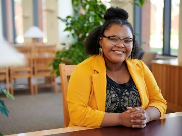 Portrait of Student Iesha-LaShay Phillips wearing yellow blazer and sitting at table in the library