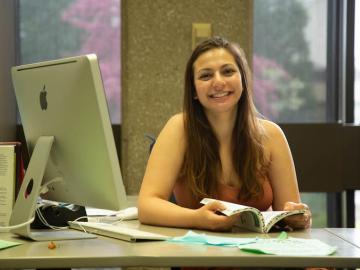 Julia Berrebi holding a book and smiling, sitting at a desk in the Writing Center