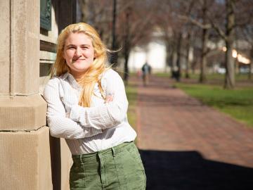 yong woman leaning against an outdoor monument.
