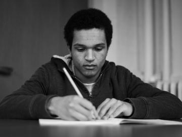 a young black man writing with a pencil in a book.