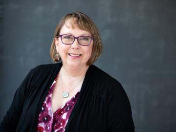 profie of woman with glasses wearing a black sweater and purple flowered blouse.