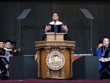Michelle Obama speaks at a podium bearing the Oberlin College seal. Dignitaries in academic robes are seated on both sides.
