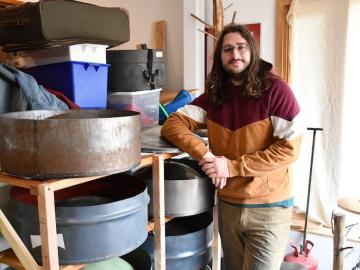 Noah Sanderson leaning against racks filled with steel pan. Photo.