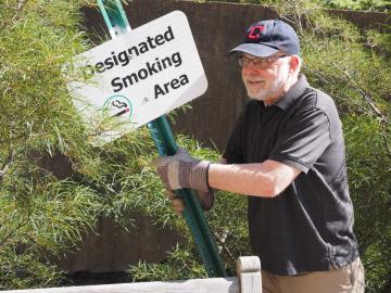A man holds a metal post with a sign reading 'Designated Smoking Area'