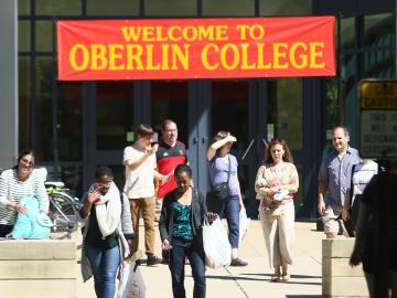 At a building entrance, people walk under a banner reading Welcome to Oberlin College.