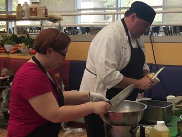 A chef and student work together in the kitchen.