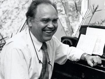 photo of smiling man seated in front of a piano