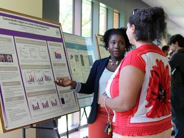 A student explains a research poster to another student.