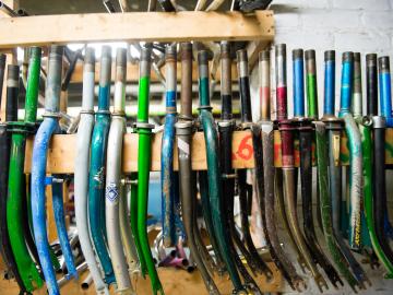 Dozens of used bicycle frame forks are lined up straddling a two-by-four.