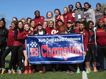 A group of about 2 dozen women pose on an athletic field. They are holding a banner that says 'North Coast Athletic Conference Champions'.